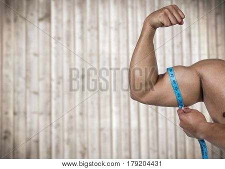 Digital composite of Muscular arm with measuring tape against blurry wood panel