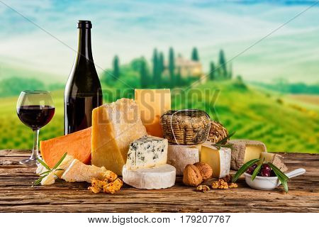 Various kind of cheese served on wooden table. Italian Toscana landscape on background. Traditional pieces of french and italy hand-made cheese. Copyspace for text