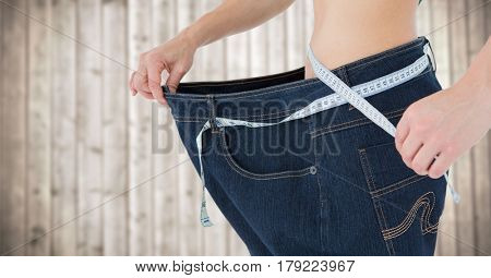 Digital composite of Woman with large pants and measuring tape against blurry wood panel