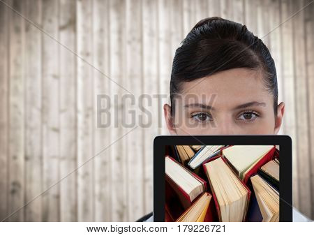 Digital composite of Woman with tablet showing standing books against blurry wood panel