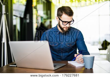 Student Busy Taking Notes Down From His New Laptop Computer While Browsing The Internet With His Mor