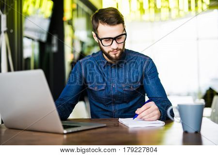 Man Taking Notes Down From His New Laptop Computer At Work In The Morning Office