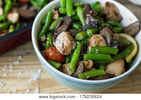 Bowl with hot salad: chicken breasts green beans red cherry tomatoes mushrooms sesame seeds