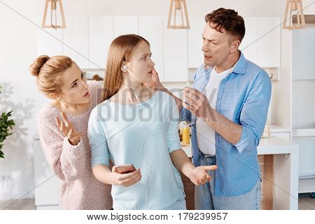 Do you hear me. Baffled young daighter holding cell phone and looking at her father who is warning her