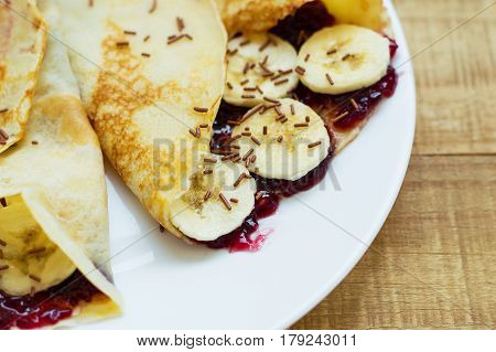 Sweet dessert: homemade thin pancakes with fresh banana slices tasty fruit jam and chocolate flavoured strands