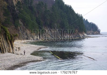 A guy walking alone along the shore near the rocks