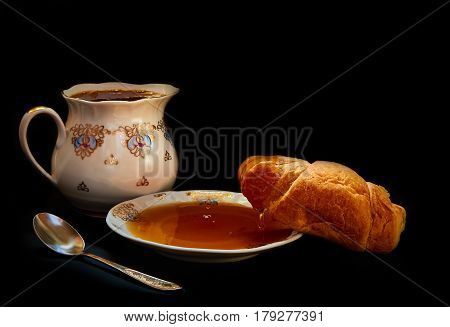 Croissant with honey and white plate on a black background