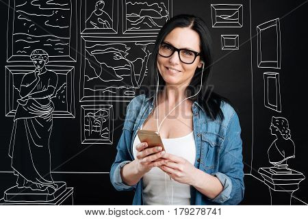 Audio guide. Intelligent nice attractive woman wearing headphones and listening to audio guide while visiting a museum