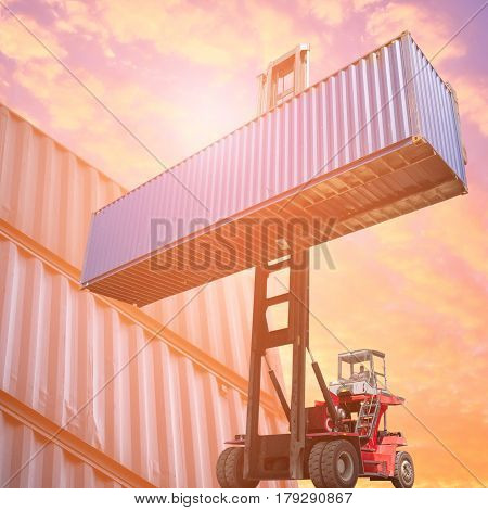 Forklift truck lifting cargo container in shipping yard or dock yard against sunrise sky with cargo container stack in background for transportation importexport and logistic industrial concept