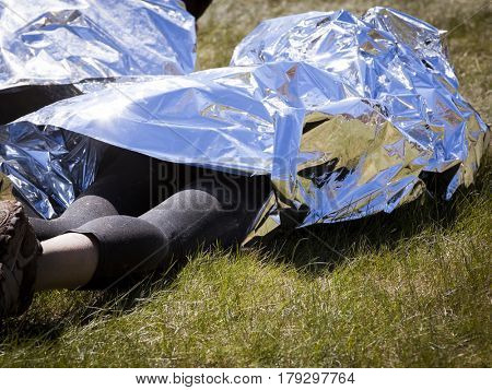 People wrapped in foil to keep warm laying on grass at the finish line after an endurance race.