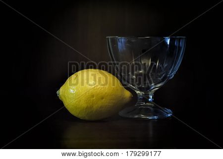 On a dark background lies a yellow lemon and next to it there is a glass small vase for ice cream.