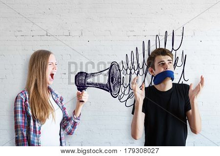 Freedom of speech concept. Young woman screaming into drawn megaphone with guy having no right to speak on white brick background