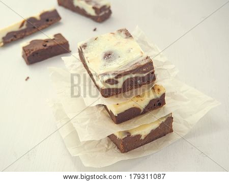 Pile of three swirl chocolate brownies. Homemade dessert upon parchment. Square pieces of brownie cheesecake. Selective focus on the front.
