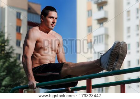 Young muscular build man doing pull ups exercises on horizontal bar outdoors, strong athletic man with naked torso training hard at sunny afternoon outside, sportsman working out. Healthy lifestyle.