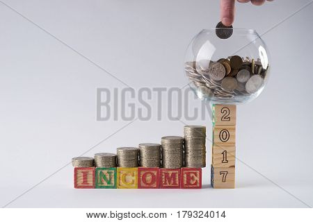 Close-up photo of Piggy bank set on wooden blocks number 2017 with Businessman's hand putting coin in money jar.Income increase concept with upward pile of coins isolated on white background.