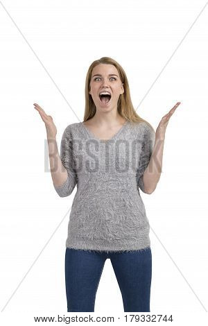 Isolated portrait of a happy blond woman wearing a gray sweater and dark blue jeans and screaming with joy with her hands in the air.