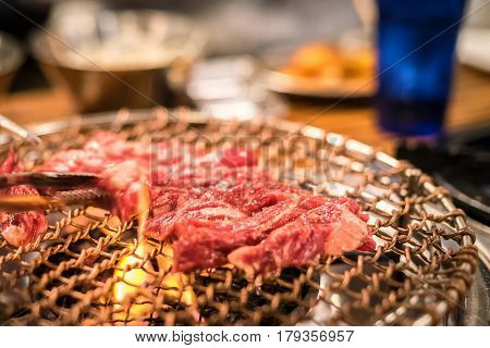 Kalbi, or Korean marinated bbq beef ribs on grill and flame in restaurant being tossed with tongs