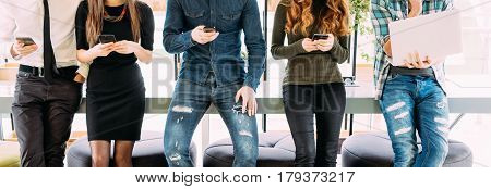 Cropped Group Of Friends Standing On Table And Browsing In Their Divices In Modern Room