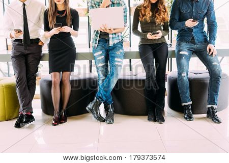 Close Up Of Group Of Friends Standing On Table And Browsing In Their Divices In Modern Room. Togethe