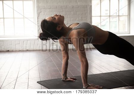 Young attractive yogi woman practicing yoga concept, standing in Purvottanasana exercise, Upward Plank pose, working out, wearing sportswear, white loft studio background, close up
