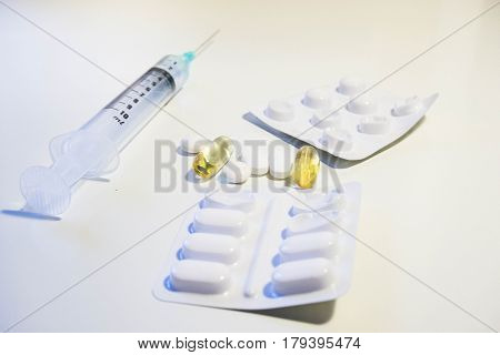 A variety of medication including a syringe with a green tip two different blister packs white pills and yellow plastic pills full of cod liver oil vitamin D supplement shot at a low angle against a white background