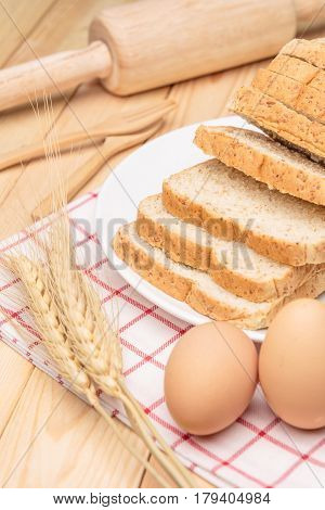 Sliced wholemeal bread on white plate with wheat ears on wooden table background Closed up