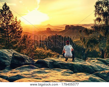 Amateur photographer takes photos with mirror camera on peak of rock. Dreamy fogy landscape spring orange pink misty sunrise in a beautiful valley below