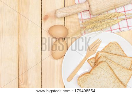 Sliced wholemeal bread on white plate with wheat ears and egg on wooden table background Top view with copy space and text.