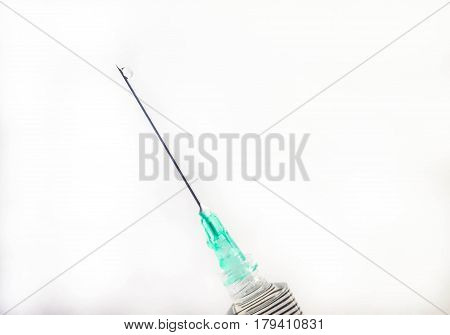 A diagonally held medical syringe with a green tip is dripping fluid from the end of its needle against a white background