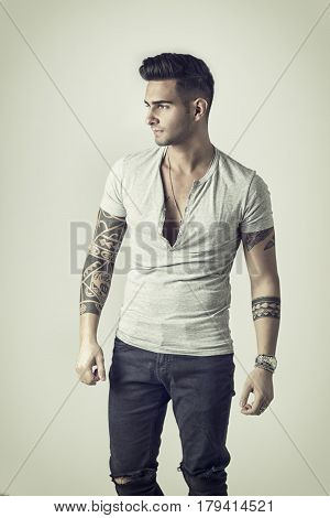 Handsome tattooed young man wearing grey t-shirt, standing against light background in studio shot
