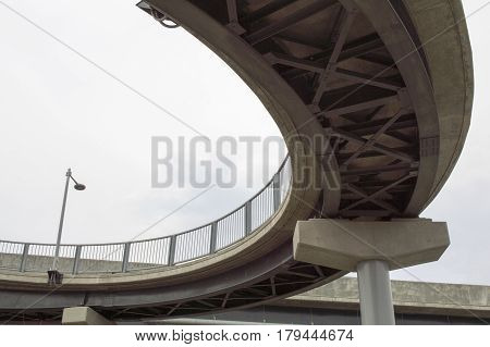 looking up from under a curved steel and concrete walkway crossing