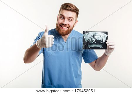 Portrait of a happy excited male medical doctor or nurse showing thumbs up gesture and holding radiograph x-ray image isolated on white background