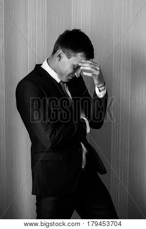 A man in a suit with a hand on the forehead is standing near the wall. Man portrait. Businessman.