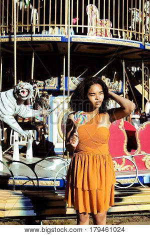 cool real modern teenage girl with candy near carousels at amusement park walking, having fun