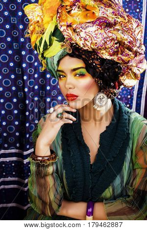 beauty bright woman with creative bright make up, many shawls on head like cubian, ethno look closeup