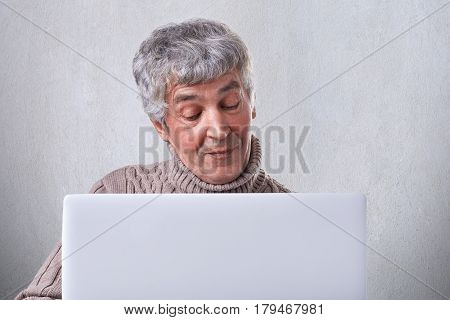 A satisfied old male having conversation online on his laptop while siting at home. An attractive mature man browsing internet using laptop computer isolated over white background.