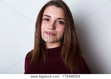 A portrait of beautiful brunette female with brown eys and charming lips having pleasant face dressed in casual sweater posing into camera while standing over white background. Beauty concept.