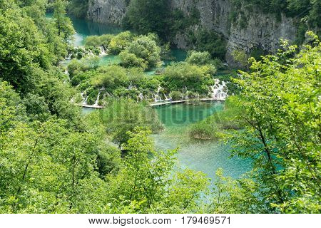 The view overlooking some of the waterfalls and lakes at Plitvice Lakes National Park with unrecognizable tourists walking along a pathway.