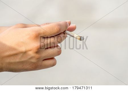 A young female had holding a rolled cigarette or marijuana joint on a blurred background.