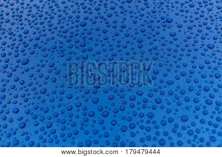 Closeup of rain drops on a blue smooth metal surface. Background or texture.