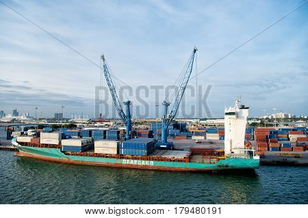 Miami Florida USA - March 18 2016: big cargo ship or barge with many shipping container in bay with lifting crane on Atlantic ocean water and cloudy blue sky sunny summer. traveling and vacation