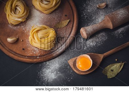 Raw homemade pasta and ingredients for cooking on a black background. Uncooked noodles with flour egg and spices. Food and culinary concept. Top view with space for text.