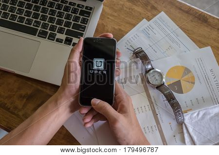 CHIANG MAITHAILAND - DEC 02 2016 : A man hand holding Uber app showing on iPhone 6s on road and black car Uber is smartphone app-based transportation network.