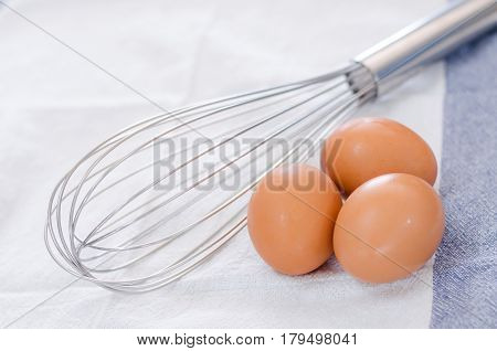 Three Eggs With Eggbeater On Wooden Table