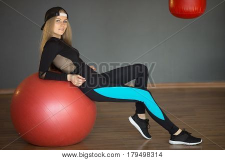 Beautiful slender girl in a sport suit in a graceful pose having a rest after training on a sport ball