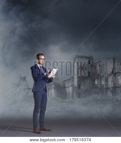 Businessman standing with computer tablet on apocalyptic background. Crisis, default, setback concept.