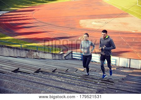 fitness, sport, exercising and lifestyle concept - happy couple running upstairs on stadium