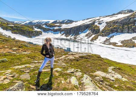 A woman turist  posing in front of frozen lake on the beautiful scenic road to the National Park Folgefonna. Norway.