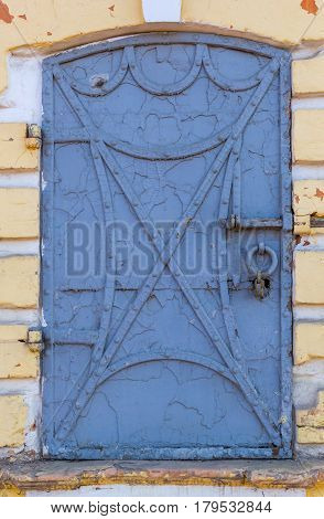 Old forged iron door with rivets and old peeling blue paint on it with yellow wall frame
