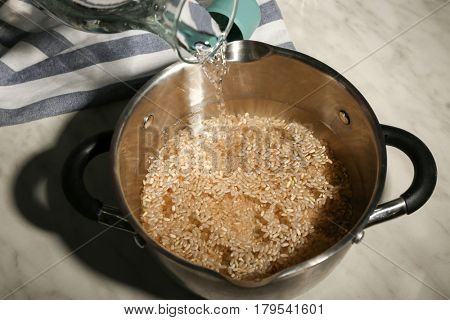 Pouring water into saucepan with brown rice on kitchen table